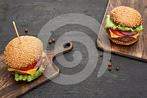 Tasty fresh cheeseburgers on wooden boards on black table