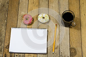 Tasty and fresh donuts and a notebook, pencils for drawing. Sketchbook and sweet biscuits on a wooden table.