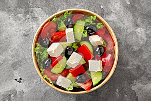 Horiatiki salad with chopped vegetables, lettuce, feta cheese and black olives in paper bowl on gray stone surface