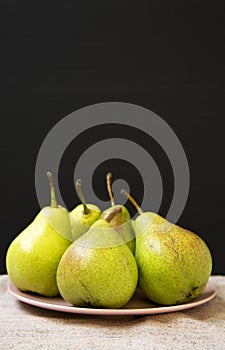 Tasty fresh pears on pink plate against black background, side view. Closeup. Selective focus.