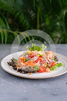 Tasty and fresh salad with raw salmon, greens, tomato, pepper, onion, carrot, olive oil.