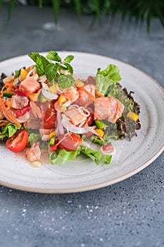 Tasty and fresh salad with raw salmon, greens, tomato, pepper, onion, carrot, olive oil.