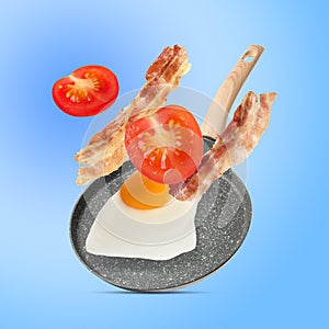 Tasty fried chicken egg, bacon and tomato falling into frying pan on light blue background