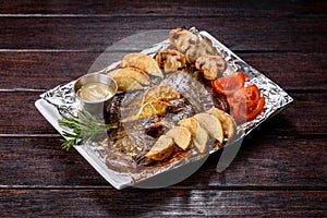 Tasty fried fish with potatoes and tomatoes on a white rectangular dish