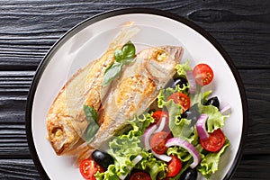 Tasty fried pink dorado or gilt-head bream fish with vegetable salad close-up on a plate. Horizontal top view