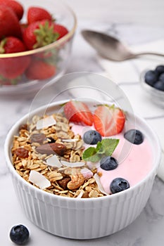 Tasty granola, yogurt and fresh berries in bowl on white table, closeup. Healthy breakfast