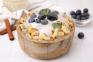 Tasty granola, yogurt and fresh berries in bowl on white tiled table, closeup. Healthy breakfast