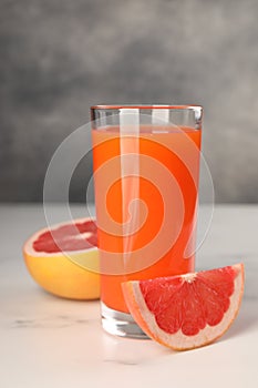 Tasty grapefruit juice in glass and fresh fruit on white table