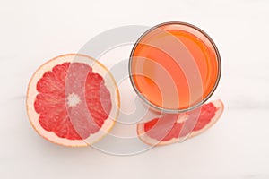 Tasty grapefruit juice in glass and slices of fresh fruit on white table, top view