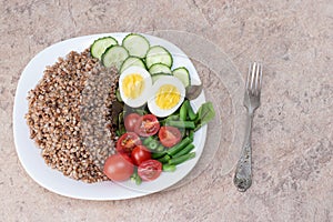 Tasty and healthy food from natural products. Salad of green vegetables, tomato and buckwheat in a white plate. Buckwheat with veg