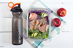 Tasty healthy lunch of vegetables, baked turkey and a bottle of water. Salad of red cabbage, spinach, apples, fresh cucumbers with