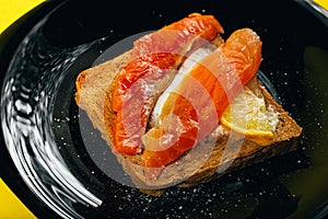 Tasty healthy toast with butter, salmon and lemon on a black glossy plate on a yellow background