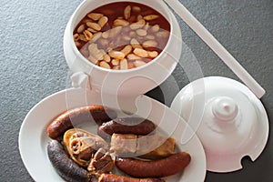 Tasty homemade asturian fabada; bowl with the beans and side dish with meat, jam, chorizo and blood sausages. Traditional photo