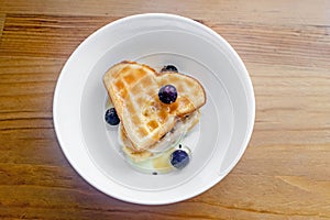 Tasty homemade Belgian waffles heart shaped on white bowl with berries and condensed milk.