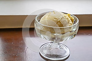 The tasty homemade cool vanilla ice cream scoop in glass cup on wood table.