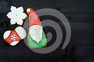 Tasty homemade gingerbread cookies with icing on dark wooden table, top view, flat lay. Christmas background with boder of santa,