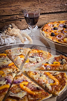 Tasty homemade pizza with salami and vegetables and a tuna pizza in the background on a rustic wooden table