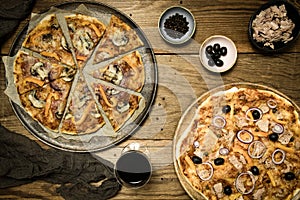 Tasty homemade pizza with salami and vegetables, a tuna pizza, red wine and black olives on a rustic wooden table