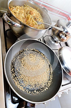 Tasty homemade sesame seeds in metal pan and noodles cooked with shrimps standing on gas stove