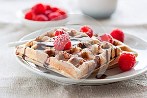 Tasty homemade waffles with raspberries and chocolate sauce ready for breakfast