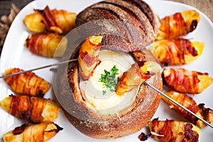 Tasty hot cheese fondue served in a bread roll with potatoes and