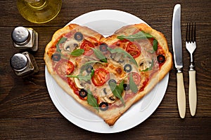 Tasty hot pizza in heart shape with chicken and mushrooms and cutlery on wooden table.