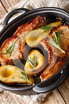 Tasty hot pork chops baked with pears and rosemary in honey sauce in a pan close-up. vertical