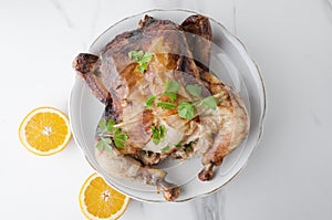 Tasty hot roasted chicken with oranges on big plate on wite marble table,top view