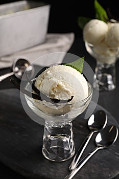 Tasty ice cream with vanilla pods in glass dessert bowl on black table