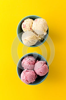 Tasty ice cream vanilla strawberry scoops in blue bowls on yellow vibrant background.