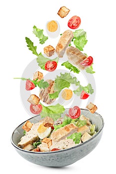 Tasty ingredients for Caesar salad falling into bowl on white background