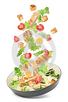 Tasty ingredients for Caesar salad falling into plate on white background