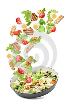 Tasty ingredients for Caesar salad falling into plate on white background