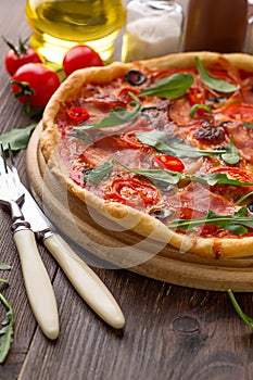 Tasty italian pizza with ham, cheese, tomatoes on cutting board with cutlery.