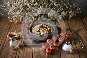 Tasty Italian spaghetti pasta with mussel, tomato and garnish on round dish and wooden plate for serving on wooden table