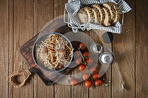 Tasty Italian spaghetti pasta with mussel, tomato, whole wheat bread and garnish on round dish and wooden plate for serving