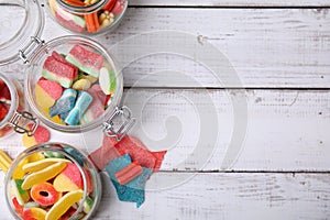 Tasty jelly candies in different jars on white wooden table, flat lay. Space for text