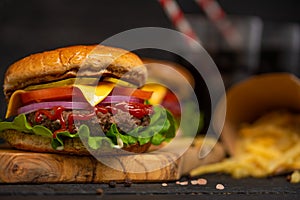 Tasty juicy beef burger, french fries and sweet soda drink on a wooden board on a black background. Cheeseburger cooked with
