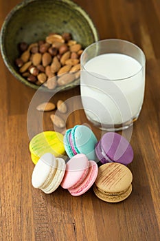 Tasty macaroons and cup of milk with almond on wooden background