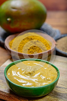 Tasty mango-curry sauce in small bowl ready to eat and bowls with mango and curry powder close up