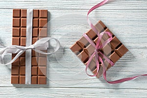 Tasty milk chocolate bars with ribbons on wooden background