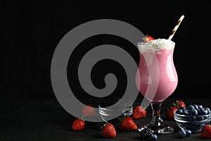 Tasty milk shake with whipped cream and berries on black slate table. Space for text