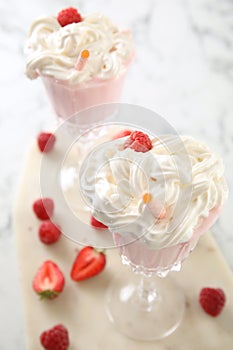 Tasty milk shake with whipped cream and fresh berries on light table, closeup