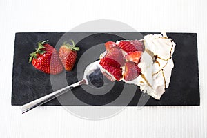 Tasty and nice piece of meringue pie with red strawberry ornament on a black slate plate