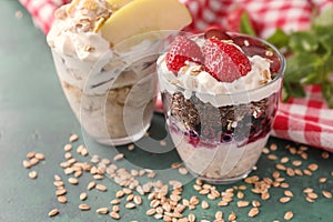 Tasty oatmeal desserts with fresh strawberries and sliced apple in glasses on color background