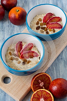 Tasty oatmeal with sicilian orange slices and raisins on blue bowls