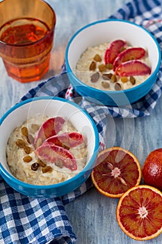 Tasty oatmeal with sicilian orange slices and raisins on blue bowls