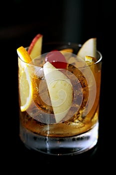 Tasty old-fashioned alcoholic cocktail with orange slice, cherry, apple and lemon peel garnish