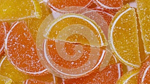 Tasty orange gummy marmalade fruit jelly, sprinkled with sugar candies, rotate slowly. Candy and sweet dessert. Top view