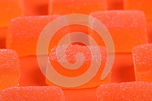 Tasty orange jelly candies on coral background, closeup